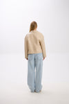 Person wearing a beige jacket and light blue jeans on a white background.