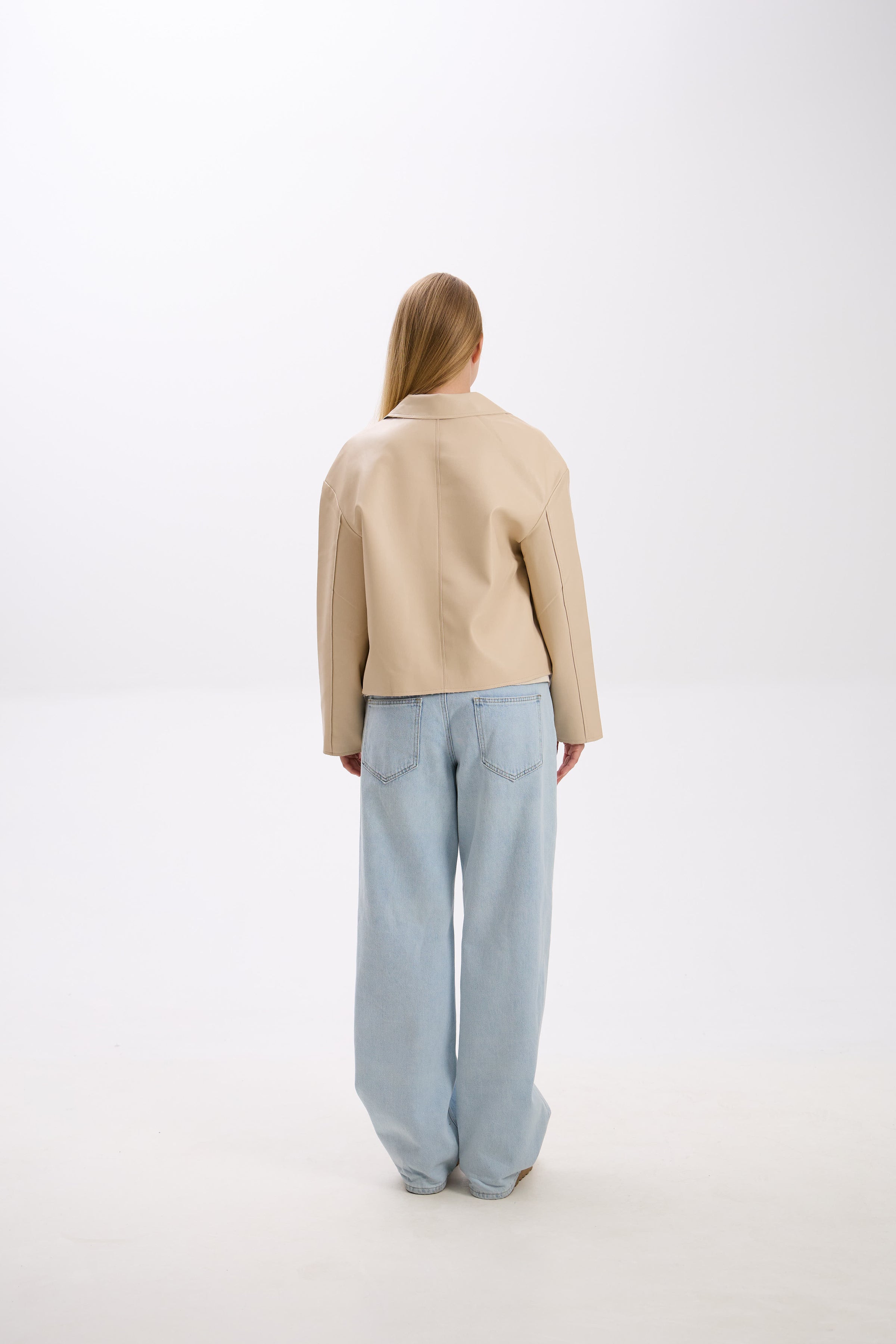 Person wearing a beige jacket and light blue jeans on a white background.