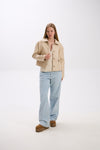 Woman wearing a beige jacket and light blue jeans on a white background.