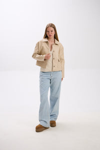 Woman wearing a beige jacket and light blue jeans on a white background.