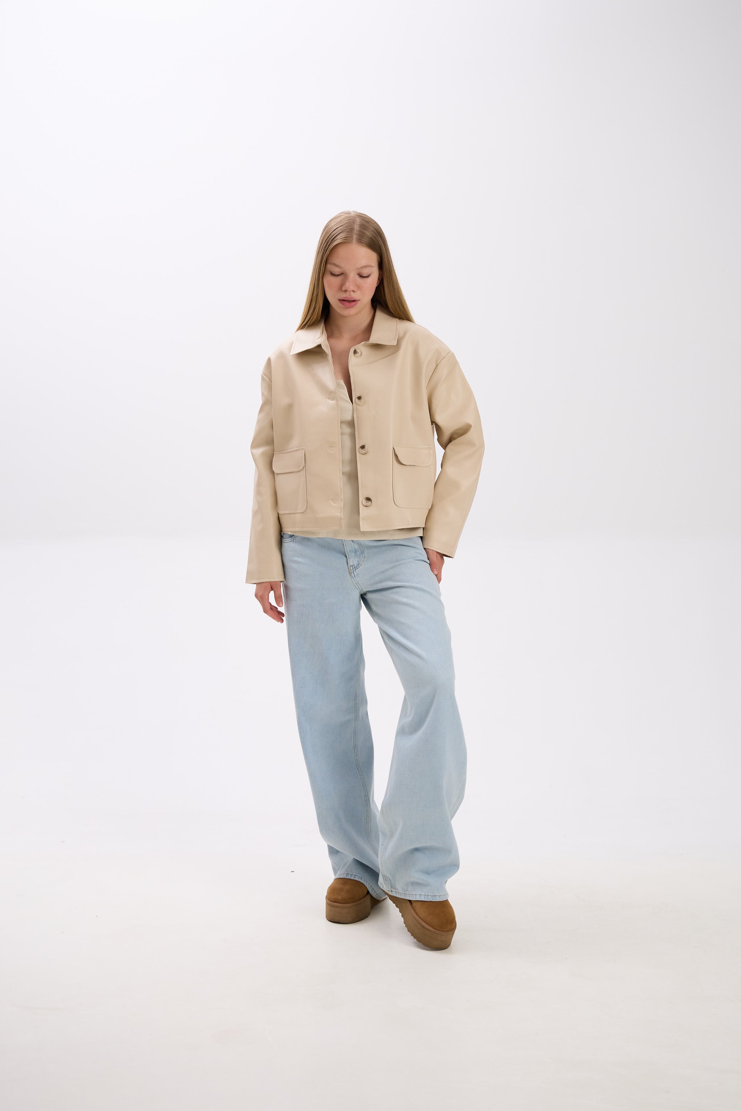 Woman wearing a beige jacket and light blue jeans on a white background.