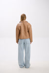 Person wearing a brown leather jacket and light blue jeans on a white background.