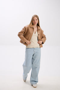 Woman wearing a beige jacket, beige top, and light blue jeans on a white background.