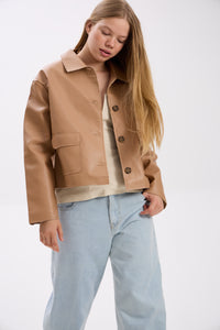 Woman wearing a tan jacket and light blue jeans on a white background.