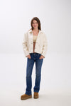 Woman wearing a white jacket, blue jeans, and brown boots on a white background.