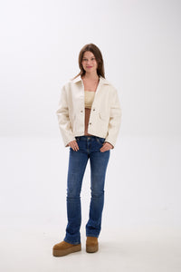 Woman wearing a white jacket, blue jeans, and brown boots on a white background.