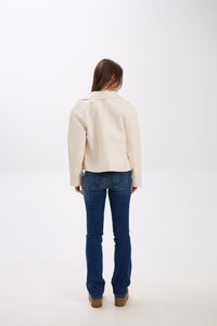 Person wearing a cream jacket and blue jeans on a white background.