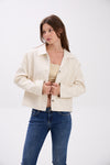 Woman wearing a cream jacket and blue jeans on a white background.