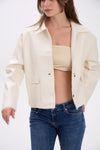 Woman wearing a beige jacket over a strapless top and blue jeans on a white background.
