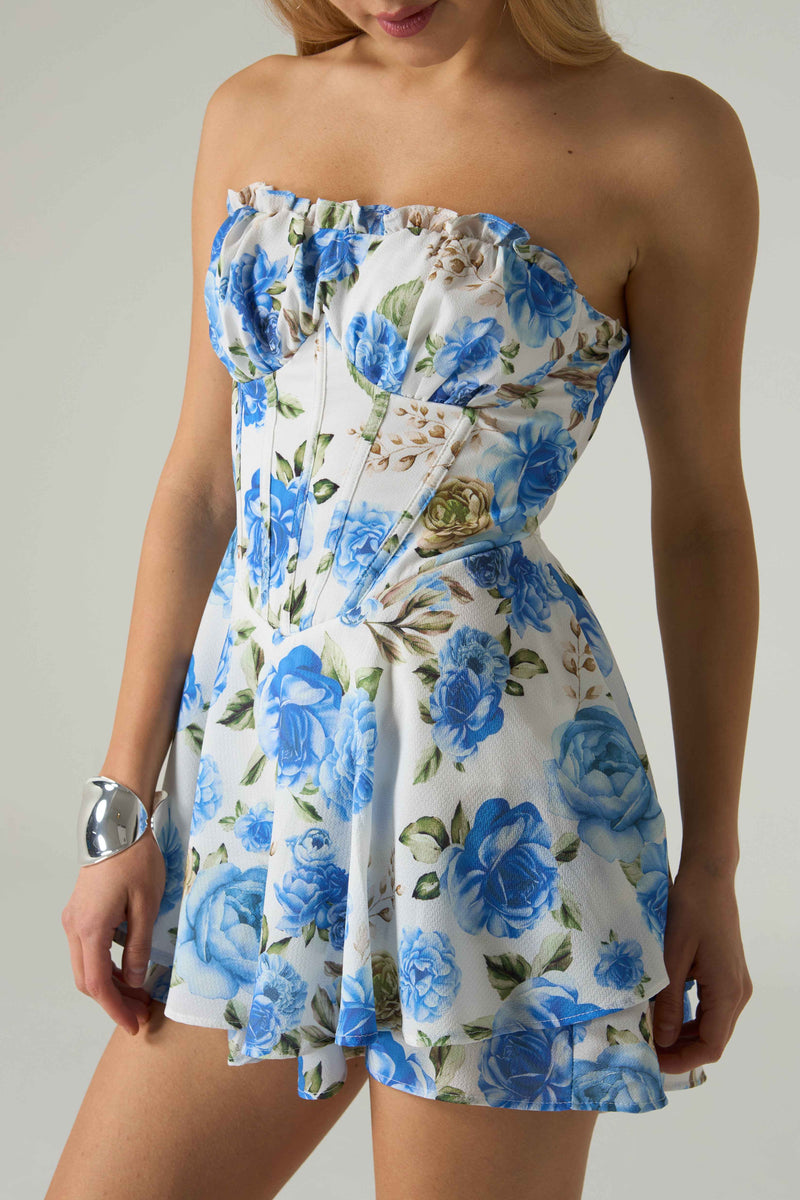 Woman wearing a strapless floral dress with blue flowers on a plain background.