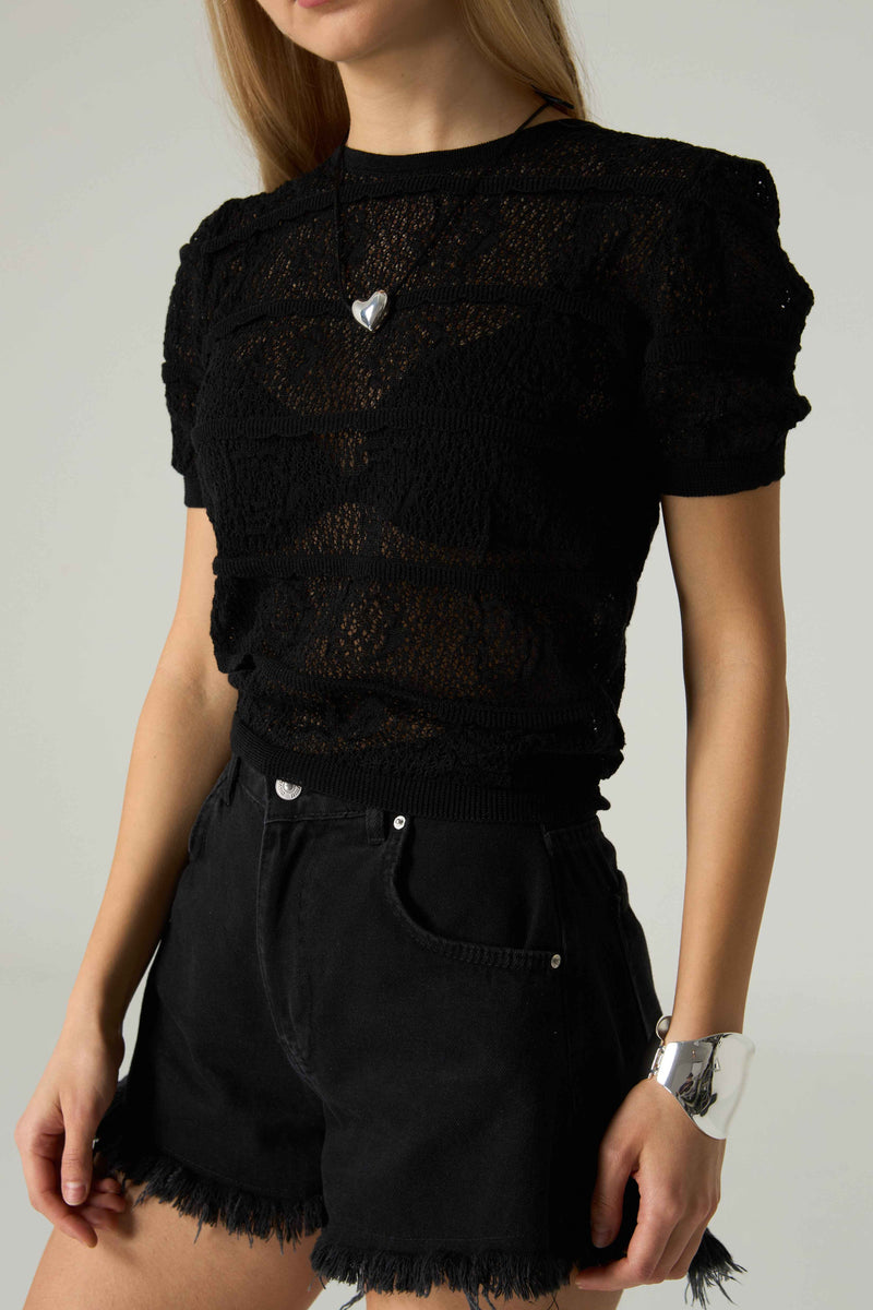 Person wearing a black lace top and black shorts on a plain background.