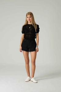 Person wearing a black outfit with sheer top and shorts on a plain background.