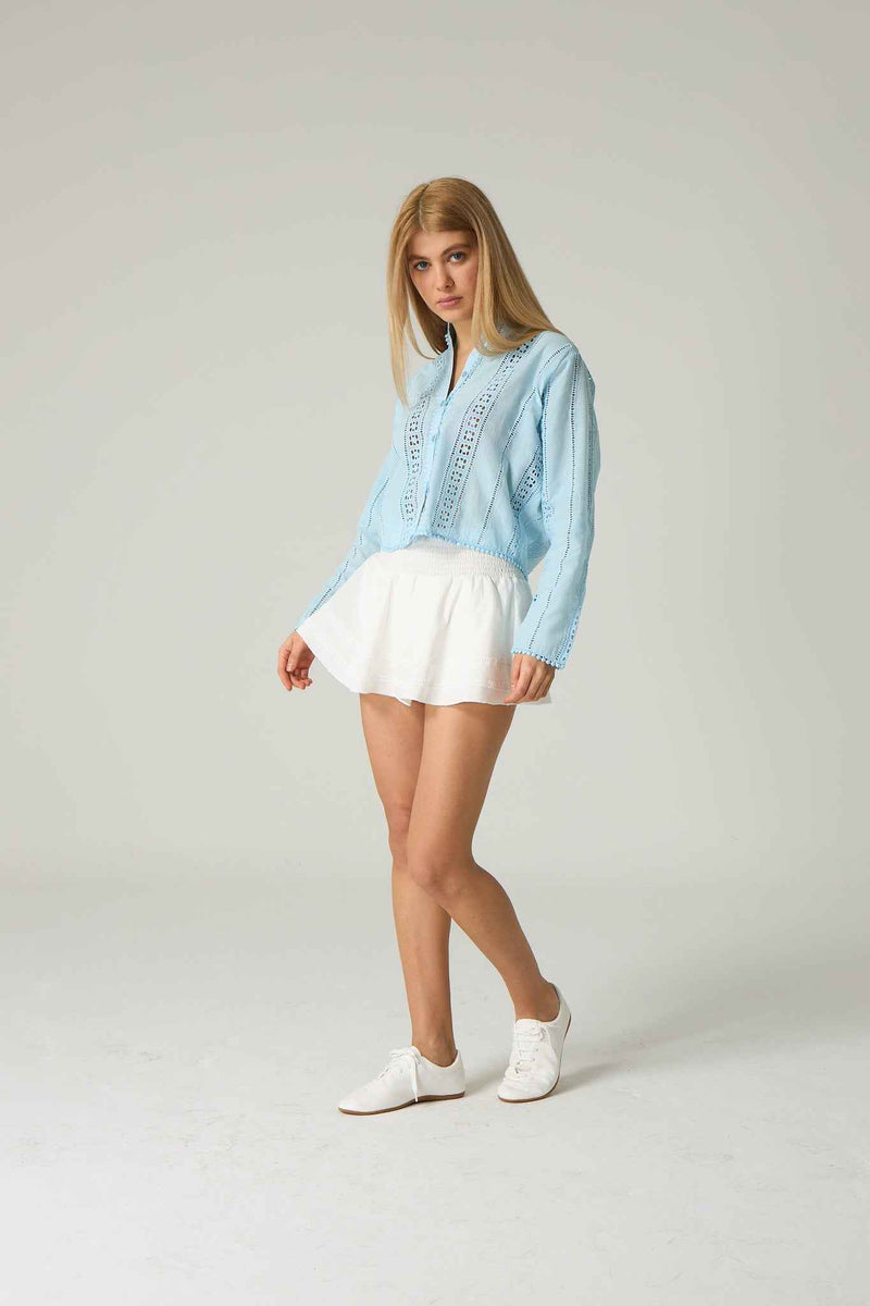 Woman wearing a light blue denim jacket and white shorts on a plain background.