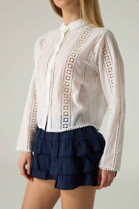 White lace blouse with long sleeves and navy tiered shorts on a plain background.