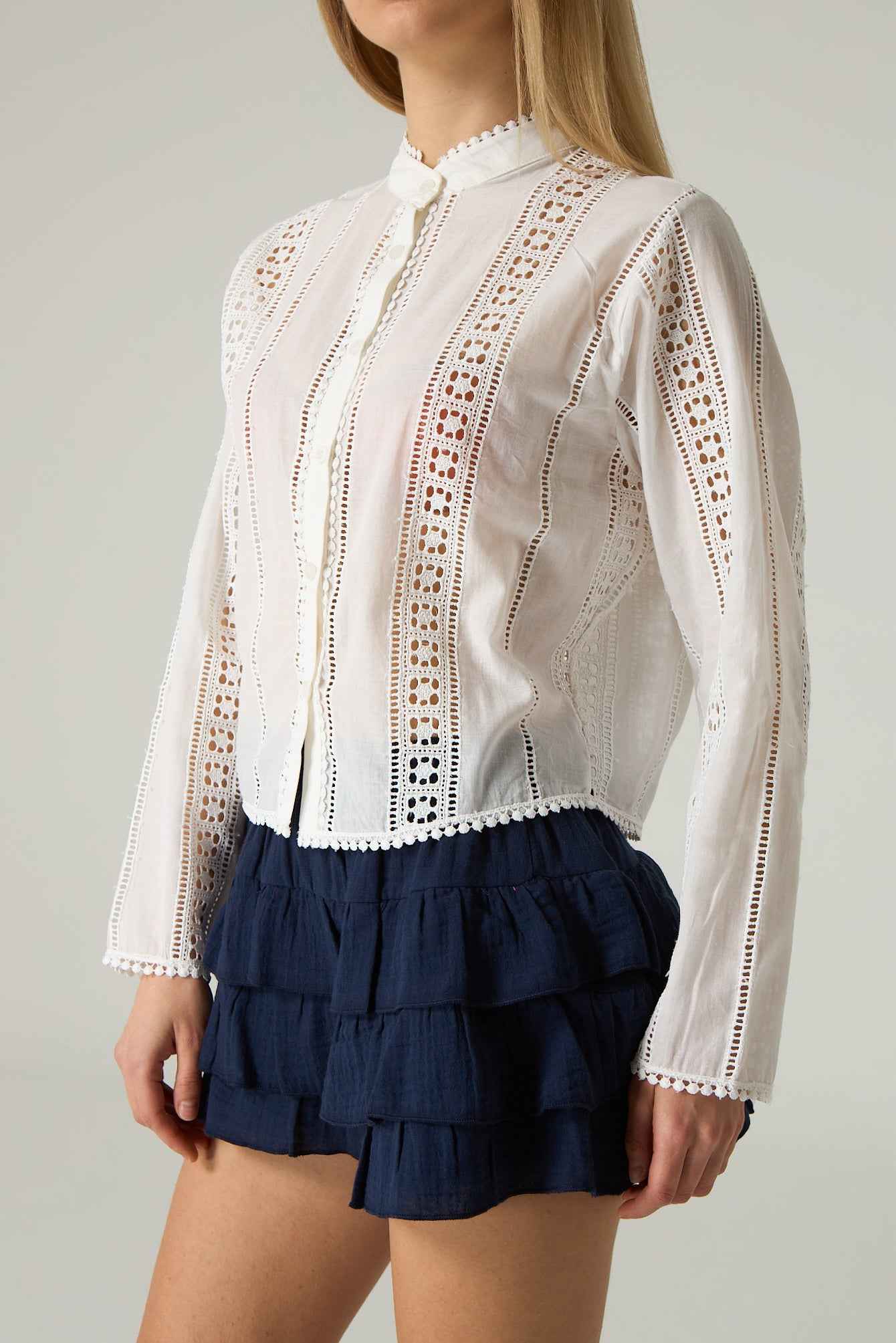 White lace blouse with long sleeves and navy tiered shorts on a plain background.