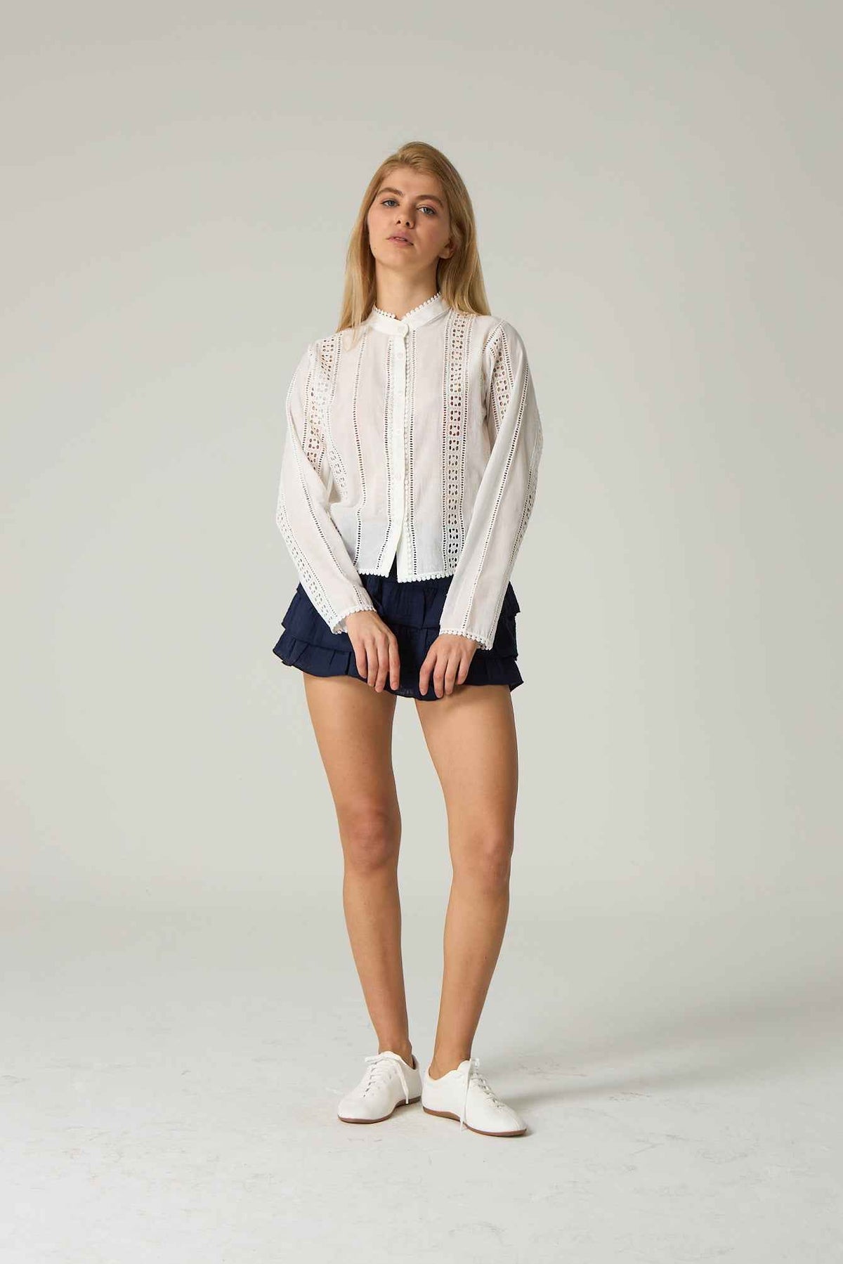 Person wearing a white lace blouse and navy shorts on a plain background.