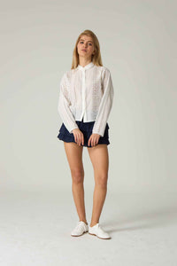 Person wearing a white lace blouse and navy shorts on a plain background.