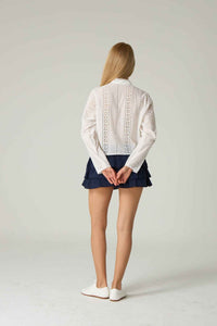 Person wearing a white lace top and navy skirt on a plain background.