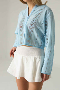 Light blue embroidered top with a white skirt on a plain background.