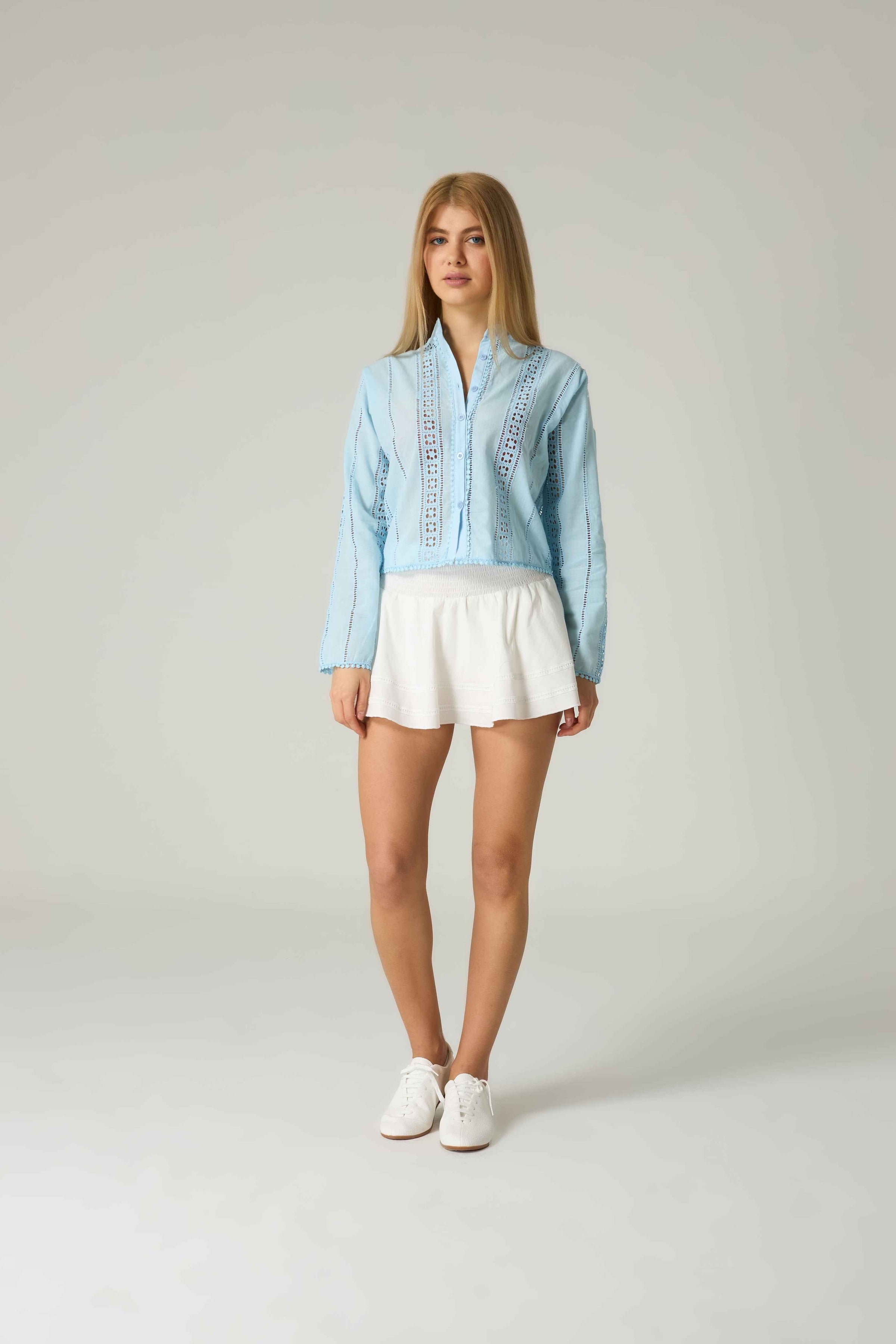 Woman wearing a light blue shirt and white shorts on a plain background.