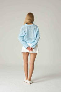 Person wearing a light blue denim jacket with lace details on a plain background.