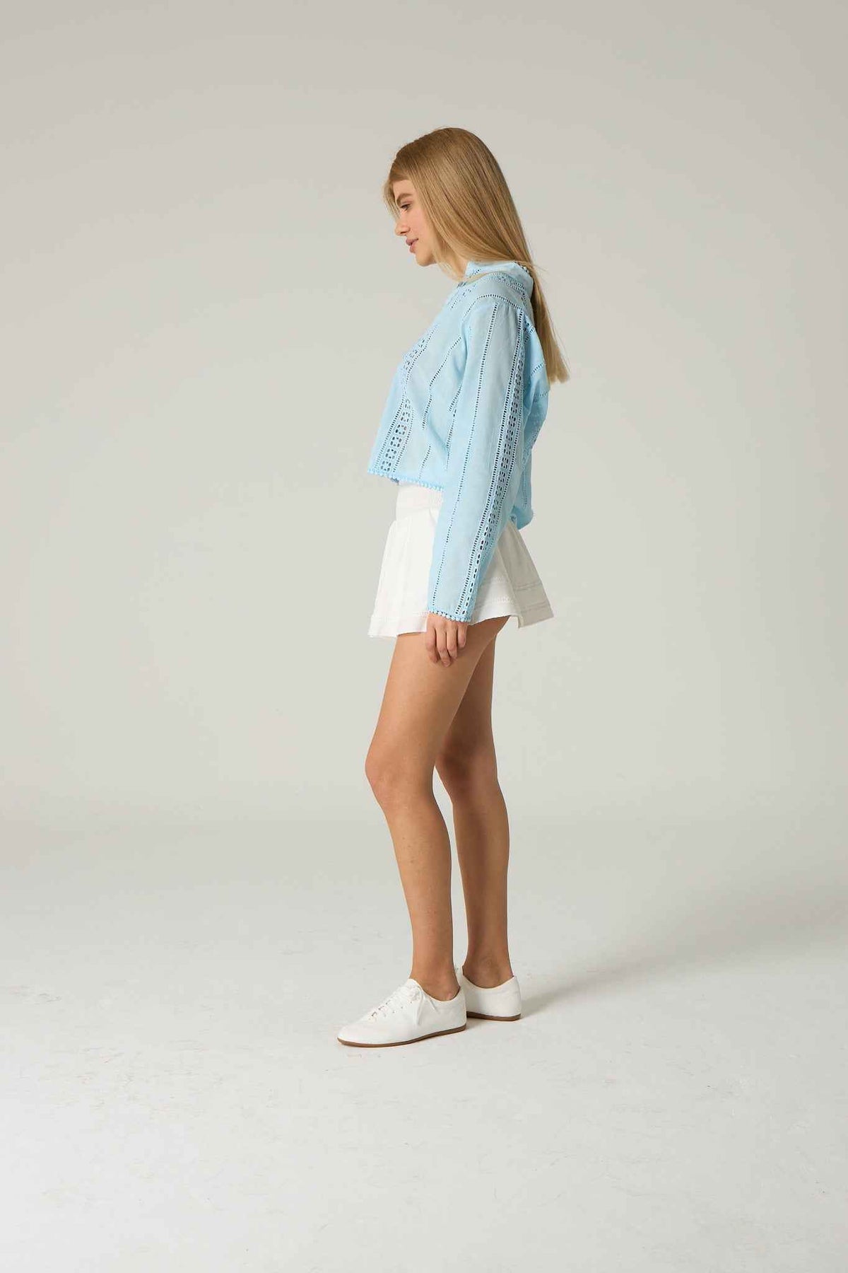 Woman wearing a light blue denim jacket over a white top and shorts on a plain background.