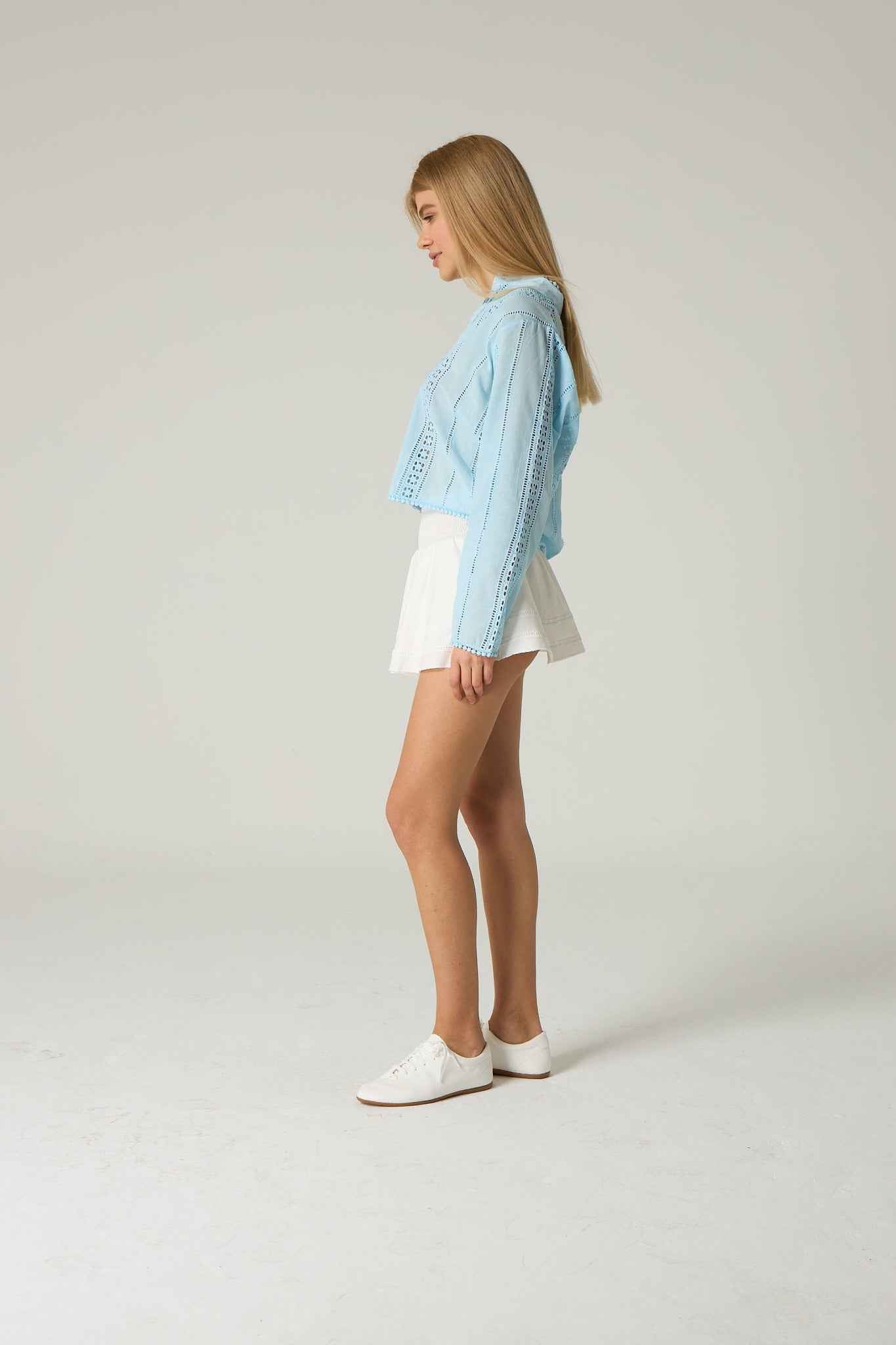 Woman wearing a light blue denim jacket over a white top and shorts on a plain background.