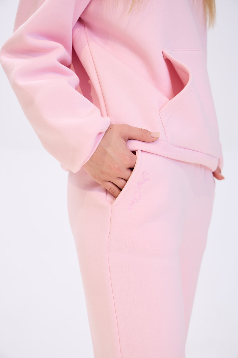 Close-up of a woman wearing light pink sweatpants with her hand in the side pocket, paired with a matching hoodie, highlighting the fabric texture and pocket detail.