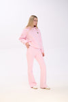Woman posing in a light pink hoodie with a small star patch on the chest, paired with matching pink flared sweatpants and white sneakers, standing against a plain white background.