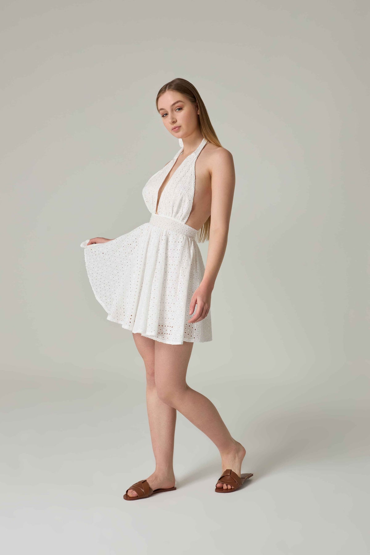 Woman wearing a white dress with cut-out design on a plain background.