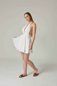 Woman wearing a white dress with cut-out design on a plain background.