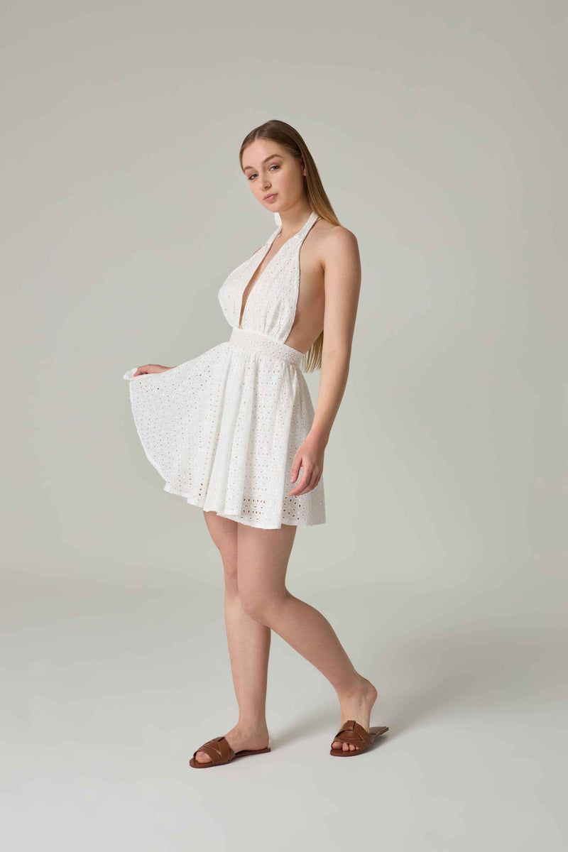 Woman wearing a white dress with cut-out design on a plain background.