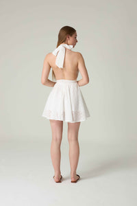 Woman wearing a white dress with a halter neck design on a plain background.