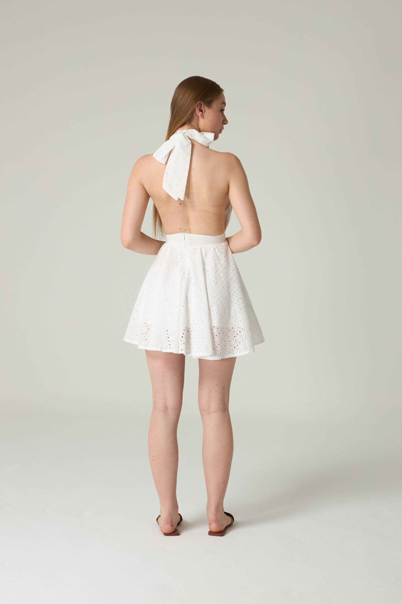 Woman wearing a white dress with a halter neck design on a plain background.