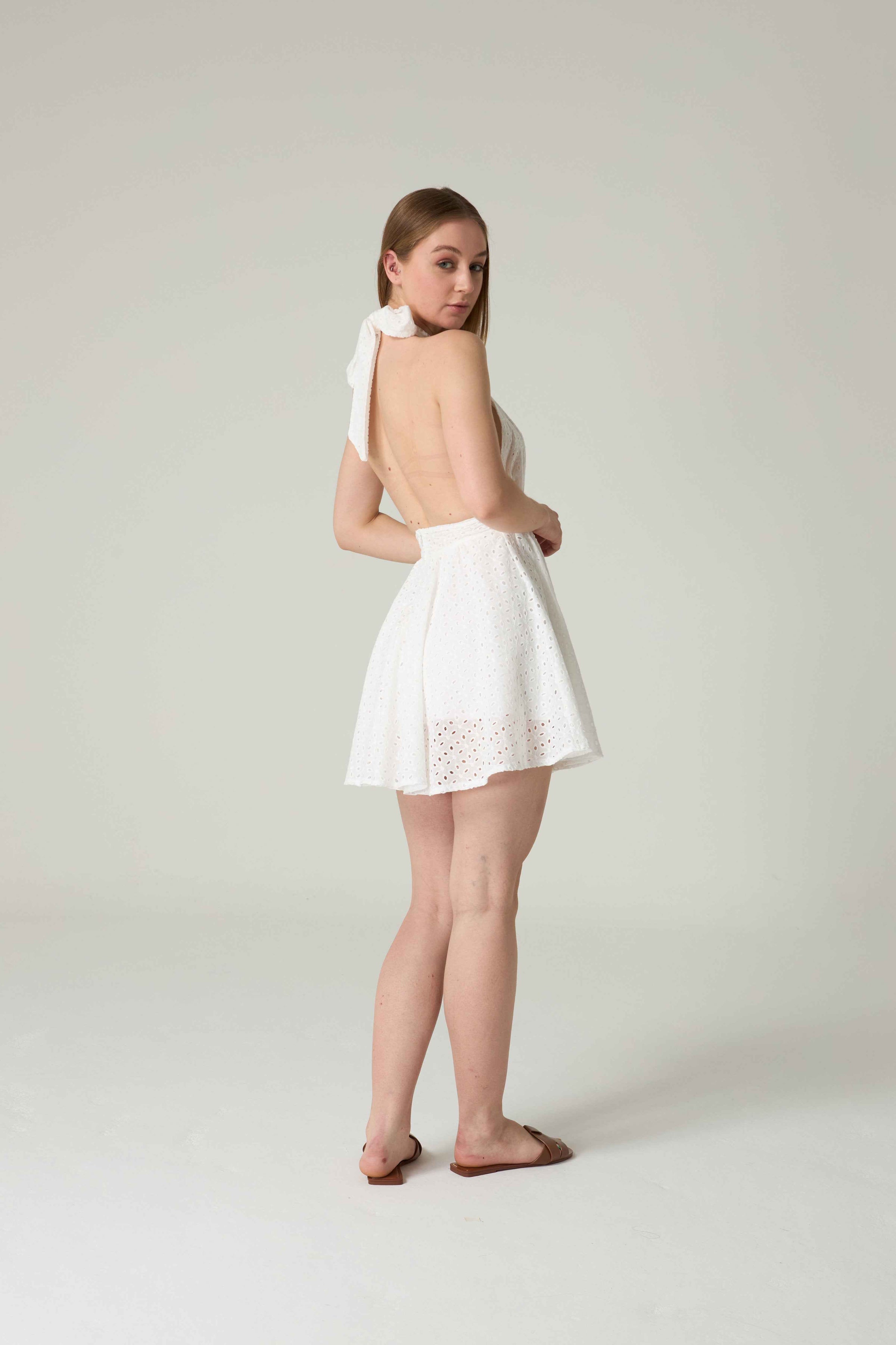 Woman wearing a white dress with a backless design on a plain background.