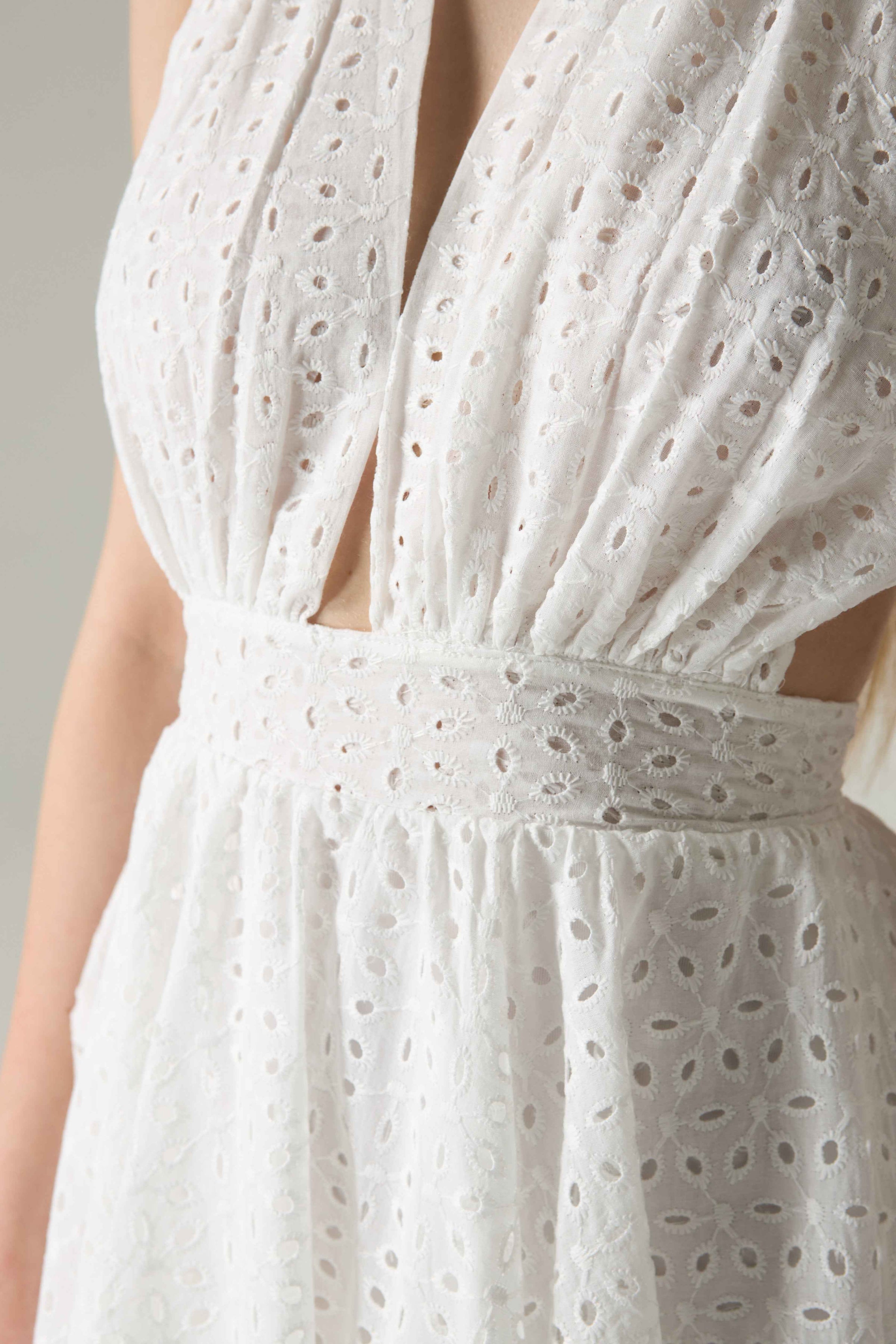 White dress with intricate cut-out pattern on a neutral background.