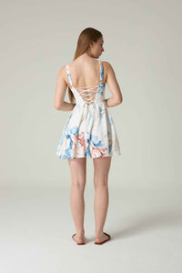 Woman wearing a floral dress with a lace-up back on a plain background.