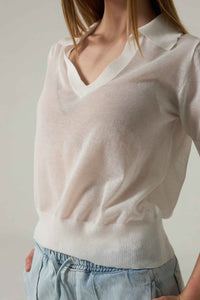 Person wearing a white sweater and light blue pants against a neutral background.