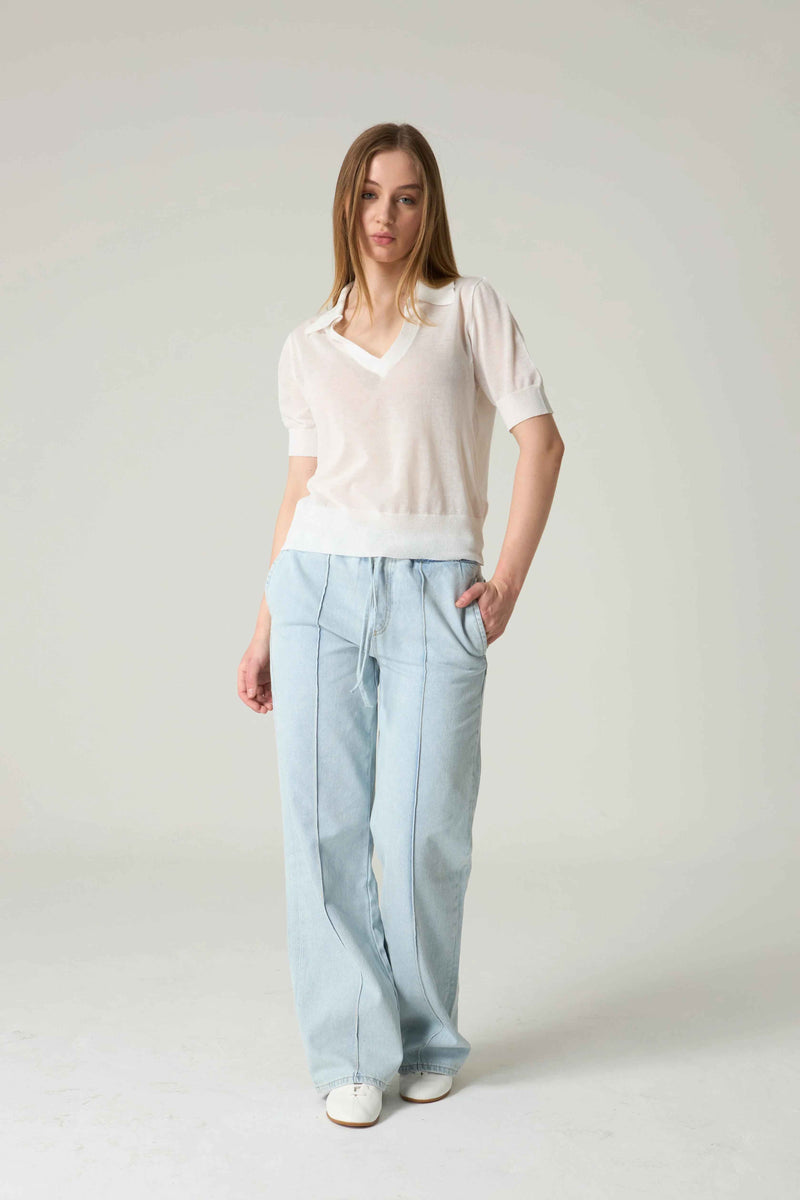 Woman wearing a white shirt and light blue pants on a plain background.