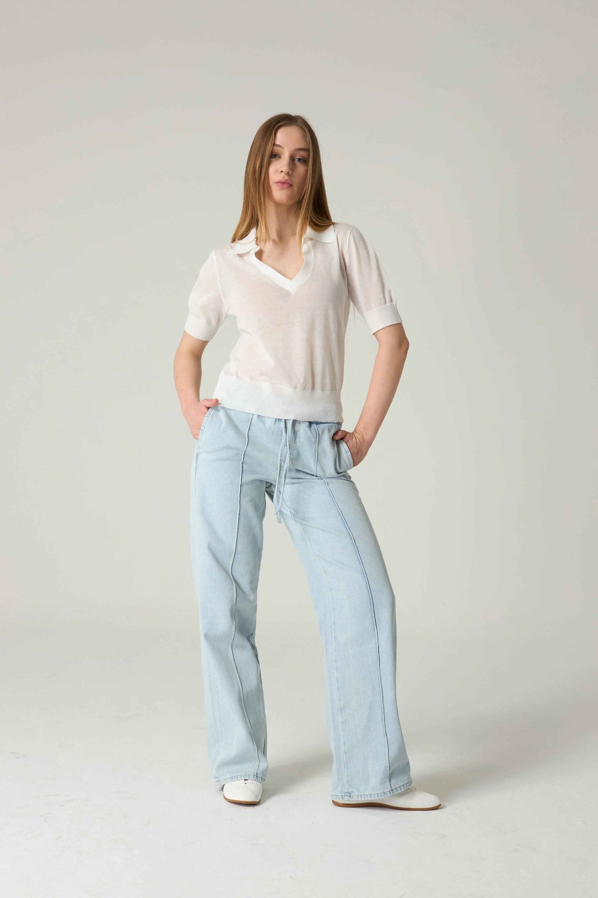 Woman wearing a light-colored blouse and light blue jeans on a plain background.