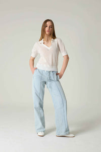 Woman wearing a light-colored blouse and light blue jeans on a plain background.