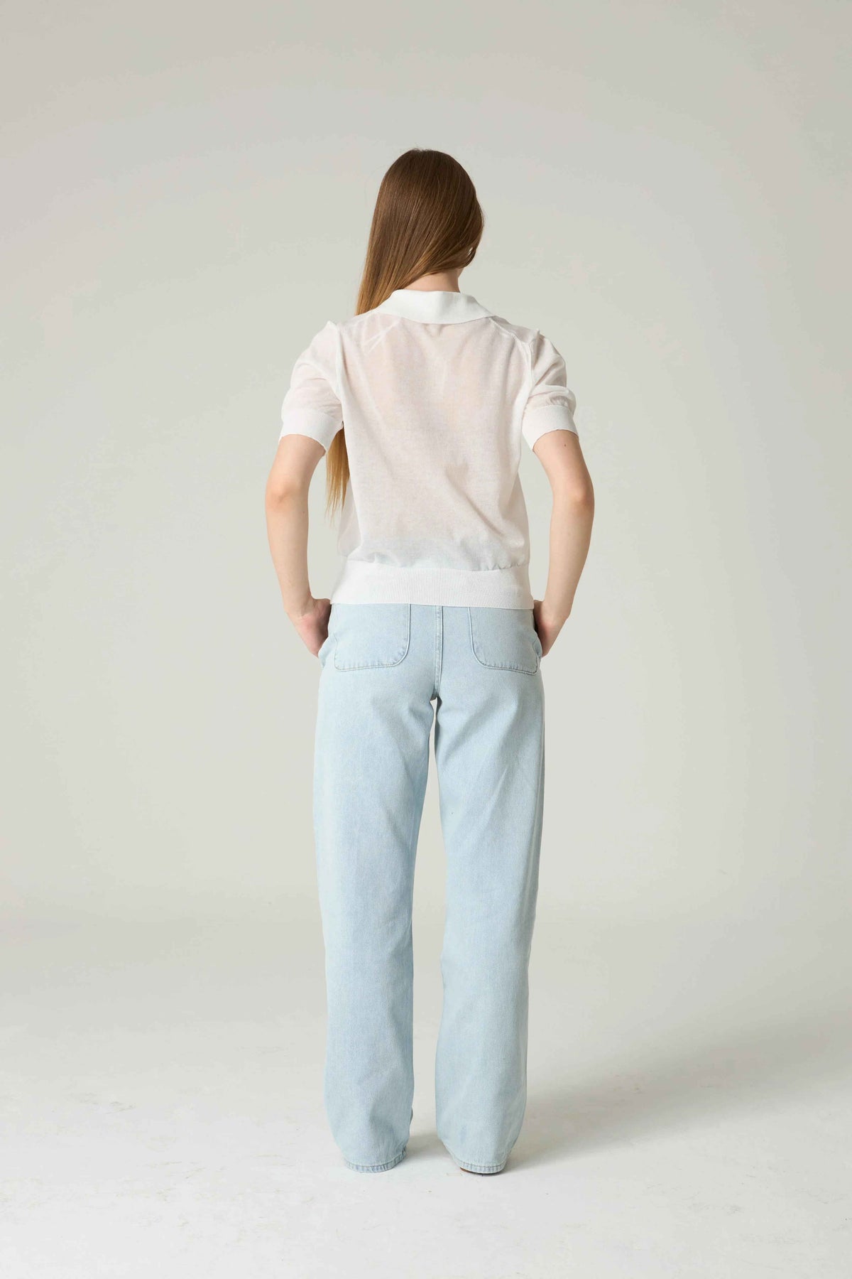 Person wearing a white polo shirt and light blue pants on a plain background.