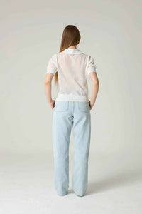 Person wearing a white polo shirt and light blue pants on a plain background.