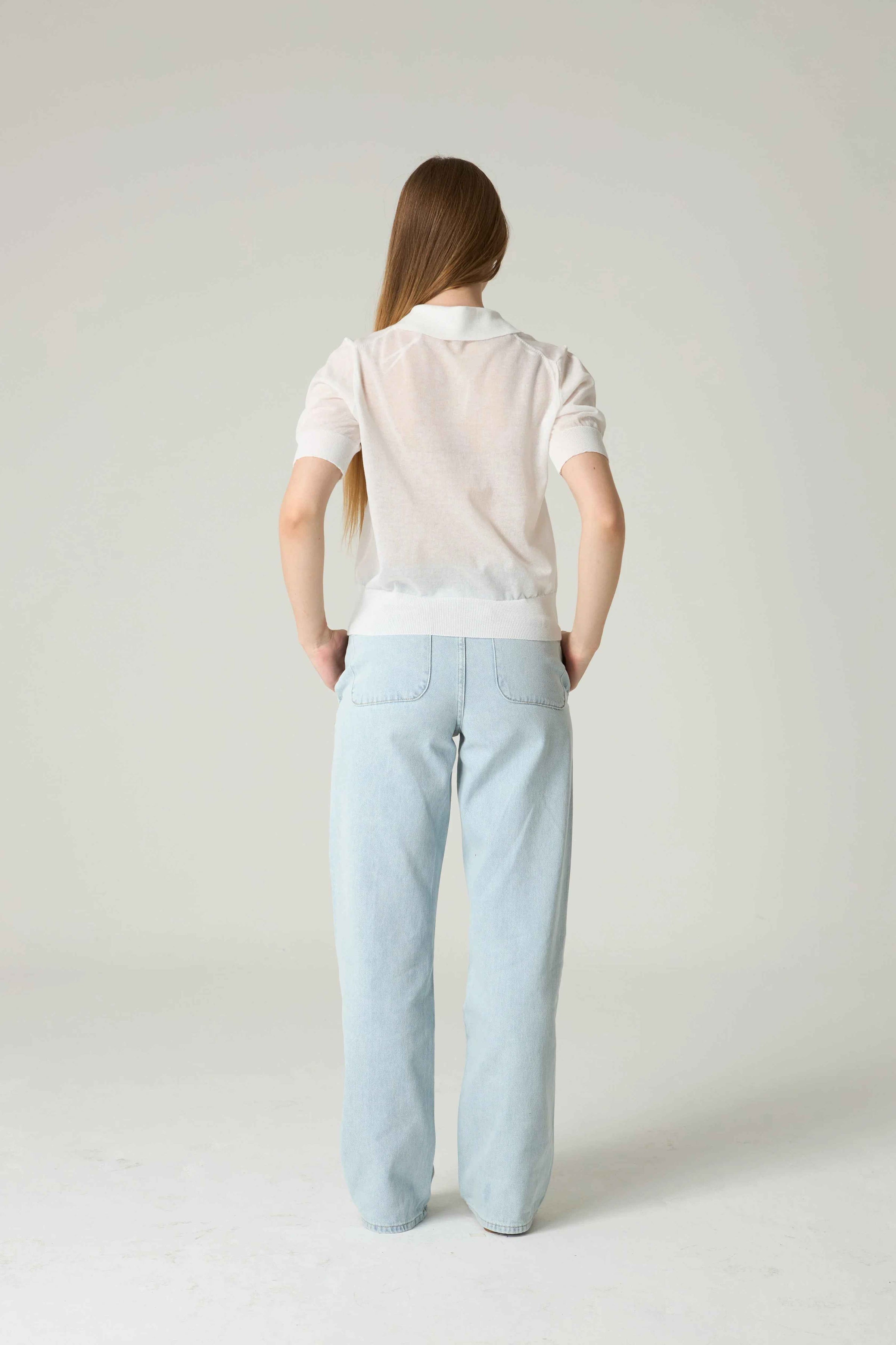 Person wearing a white polo shirt and light blue pants on a plain background.