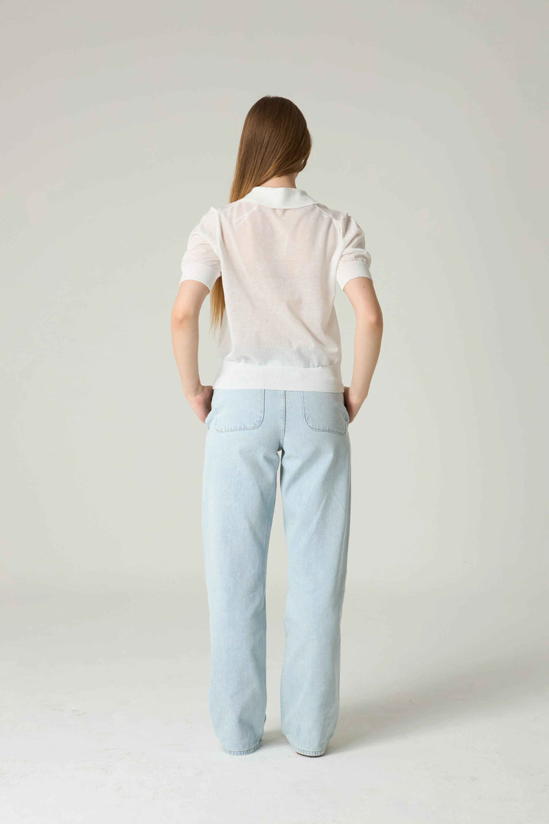 Person wearing a white polo shirt and light blue pants on a plain background.