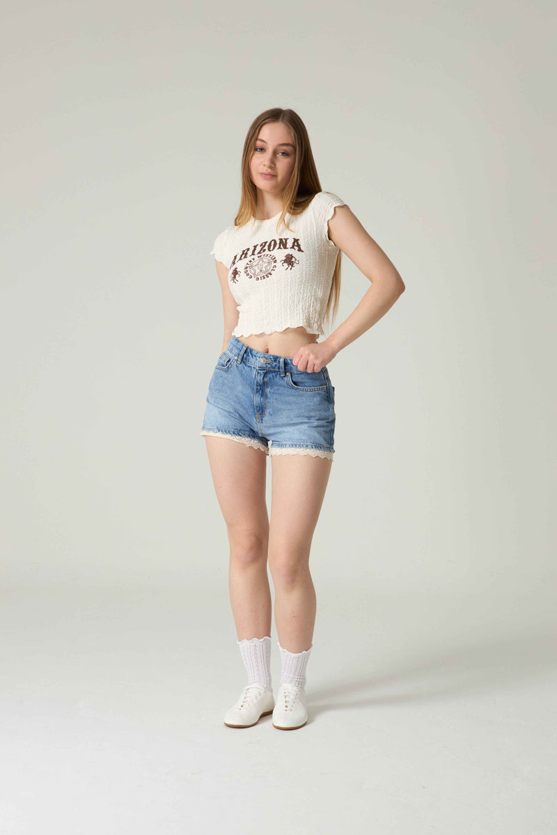 Woman wearing a white 'Arizona' t-shirt and blue denim shorts on a plain background.