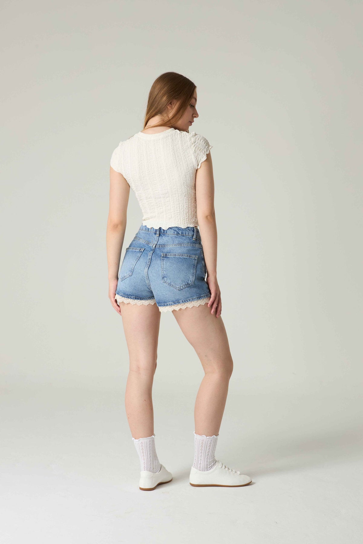 Woman wearing a white top and denim shorts on a plain background.