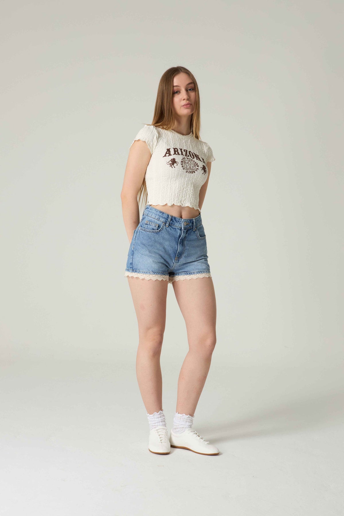 Woman wearing a white t-shirt with 'Arizona' print and blue denim shorts on a plain background.