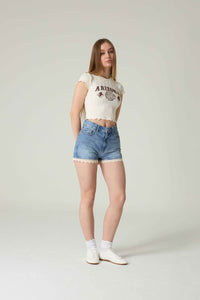 Woman wearing a white t-shirt with 'Arizona' print and blue denim shorts on a plain background.
