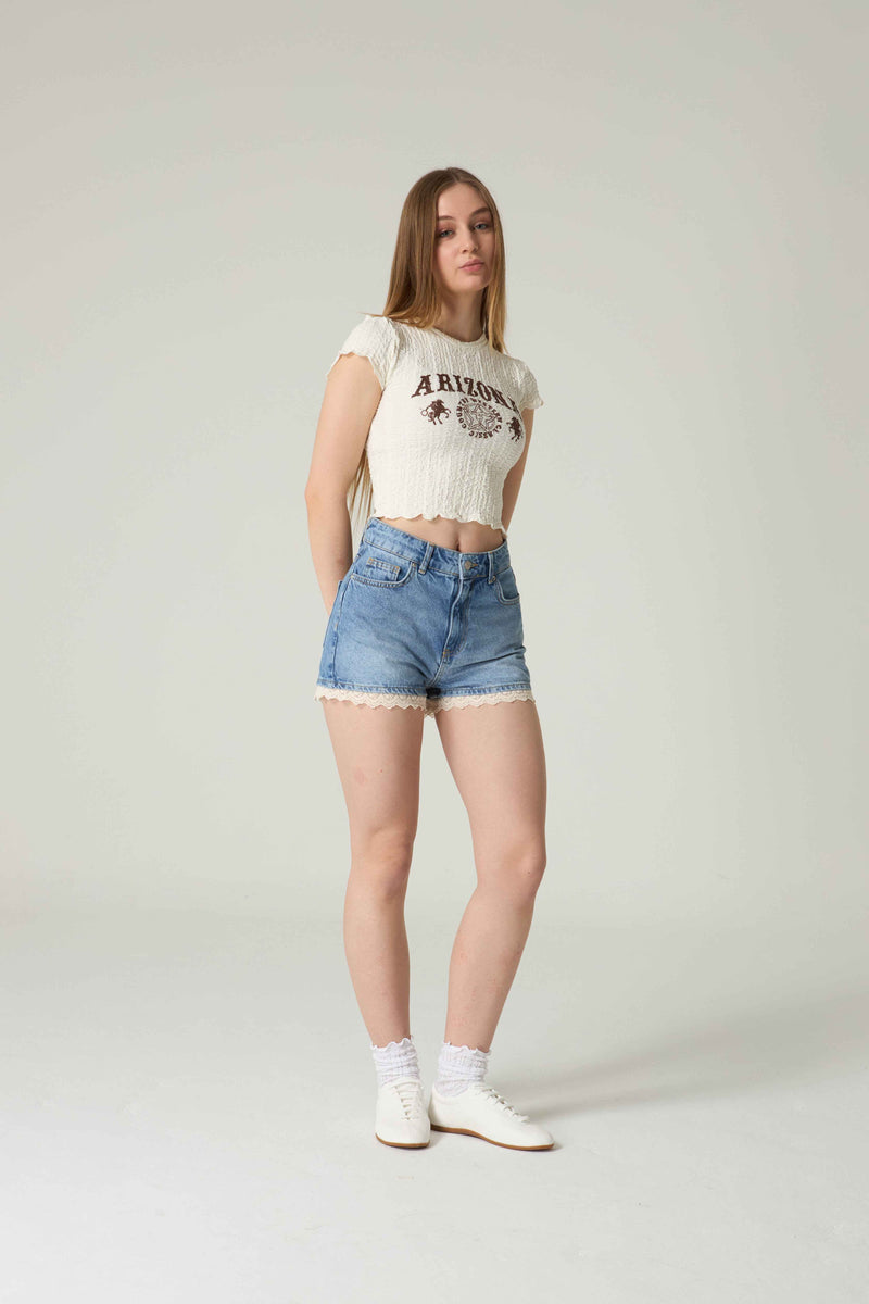 Woman wearing a white t-shirt with 'Arizona' print and blue denim shorts on a plain background.
